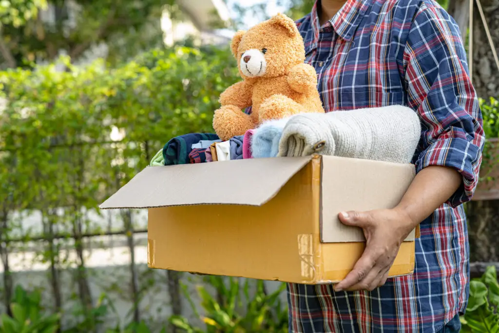 Holding clothing donation box with used clothes and teddy bear
